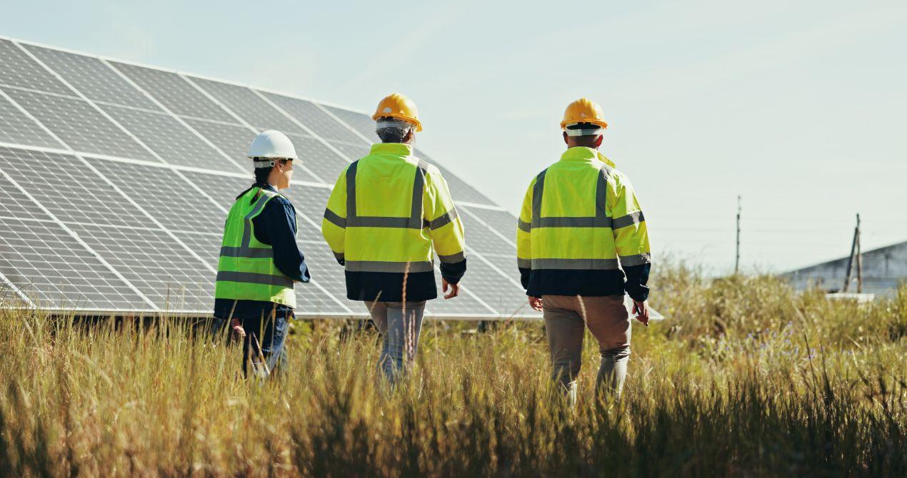 Drei Personen mit Schutzkleidung gehen entlang einer Anlage mit Glas glas photovoltaik module im Feld