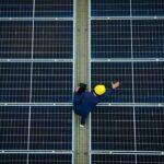 Techniker mit Helm inspiziert Glas glas photovoltaik module auf grosser Solaranlage von oben