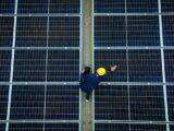 Techniker mit Helm inspiziert Glas glas photovoltaik module auf grosser Solaranlage von oben