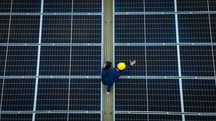 Techniker mit Helm inspiziert Glas glas photovoltaik module auf grosser Solaranlage von oben
