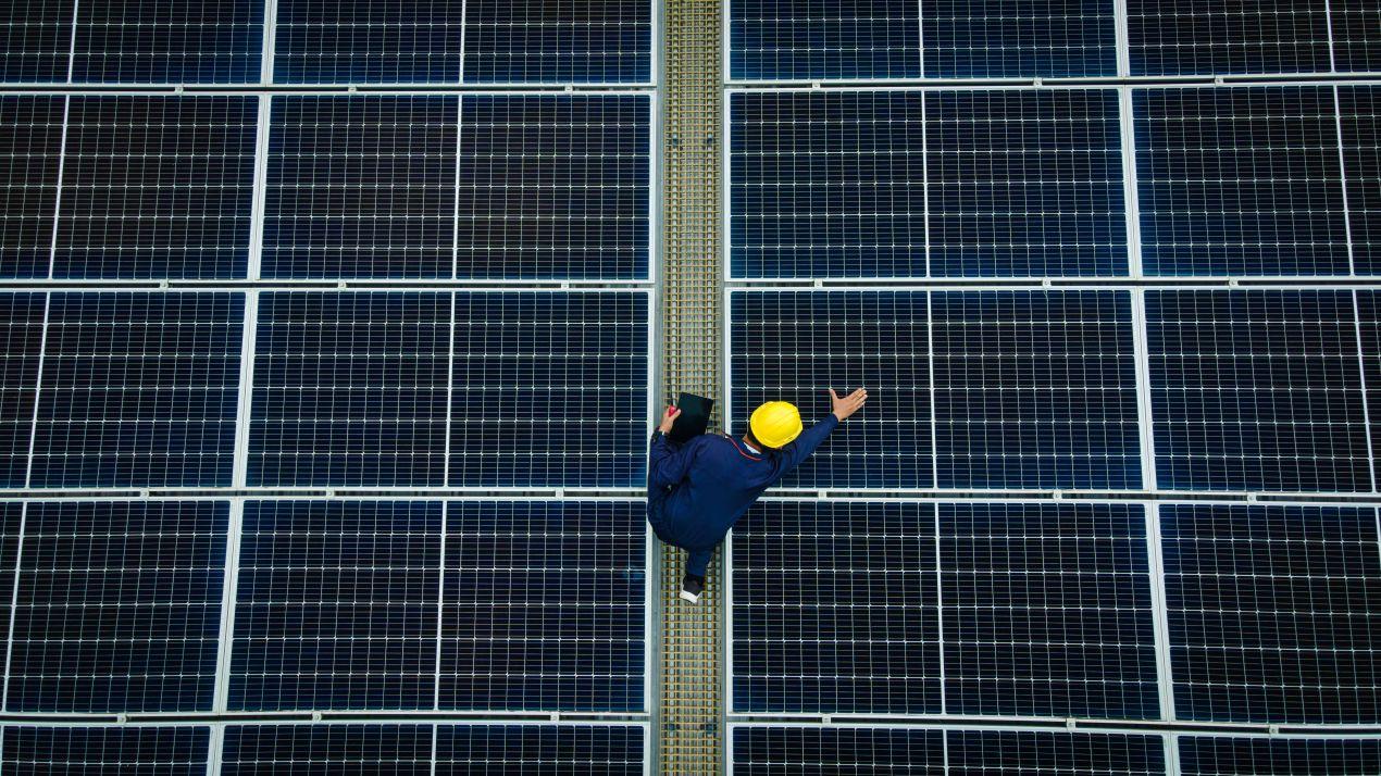 Techniker mit Helm inspiziert Glas glas photovoltaik module auf grosser Solaranlage von oben