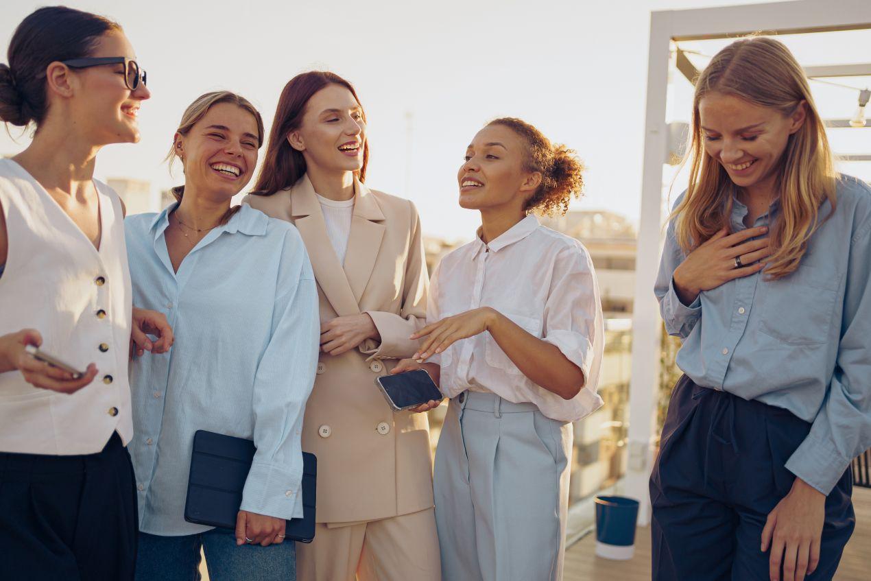 Gruppe junger Frauen lacht bei einem Afterwork-Event auf einer sonnigen Dachterrasse – ideale Firmenevent Location für informellen Austausch