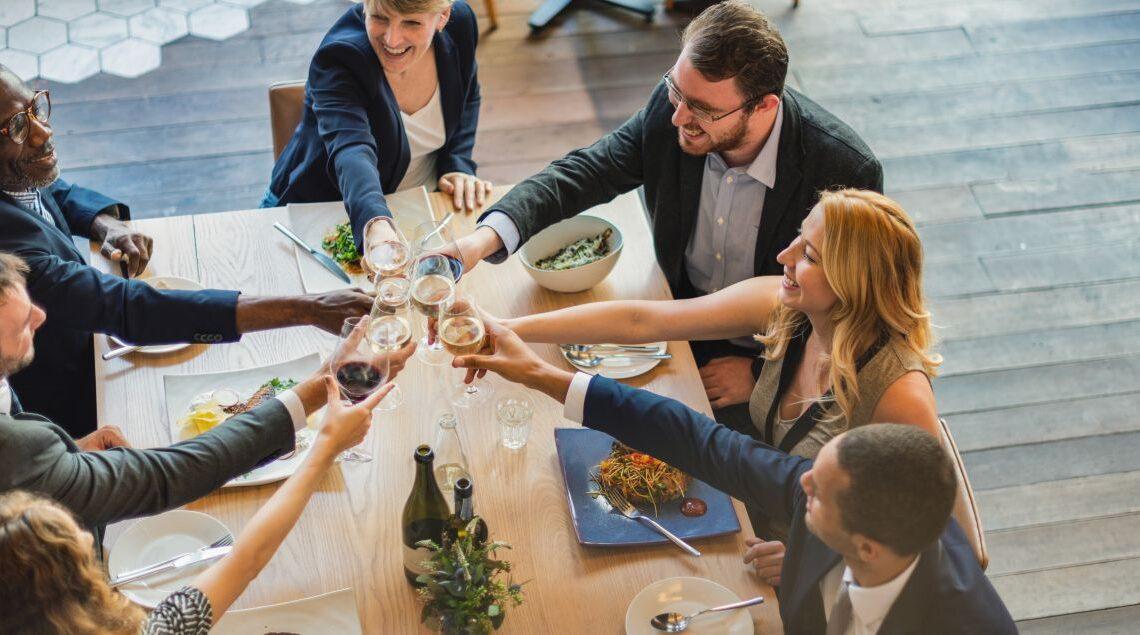 Gruppe von Kollegen bei einem festlichen Abendessen in einer eleganten Firmenevent Location mit Holzfussboden und modernem Ambiente