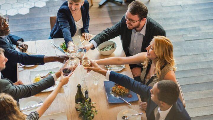 Gruppe von Kollegen bei einem festlichen Abendessen in einer eleganten Firmenevent Location mit Holzfussboden und modernem Ambiente