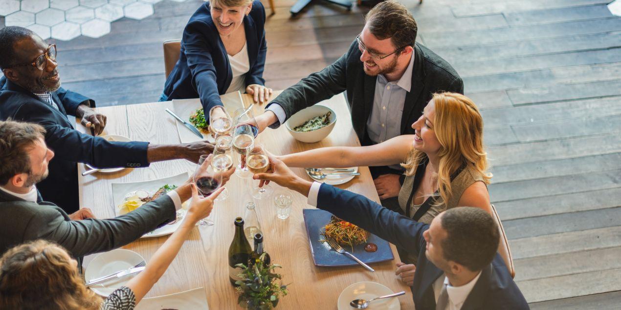 Gruppe von Kollegen bei einem festlichen Abendessen in einer eleganten Firmenevent Location mit Holzfussboden und modernem Ambiente