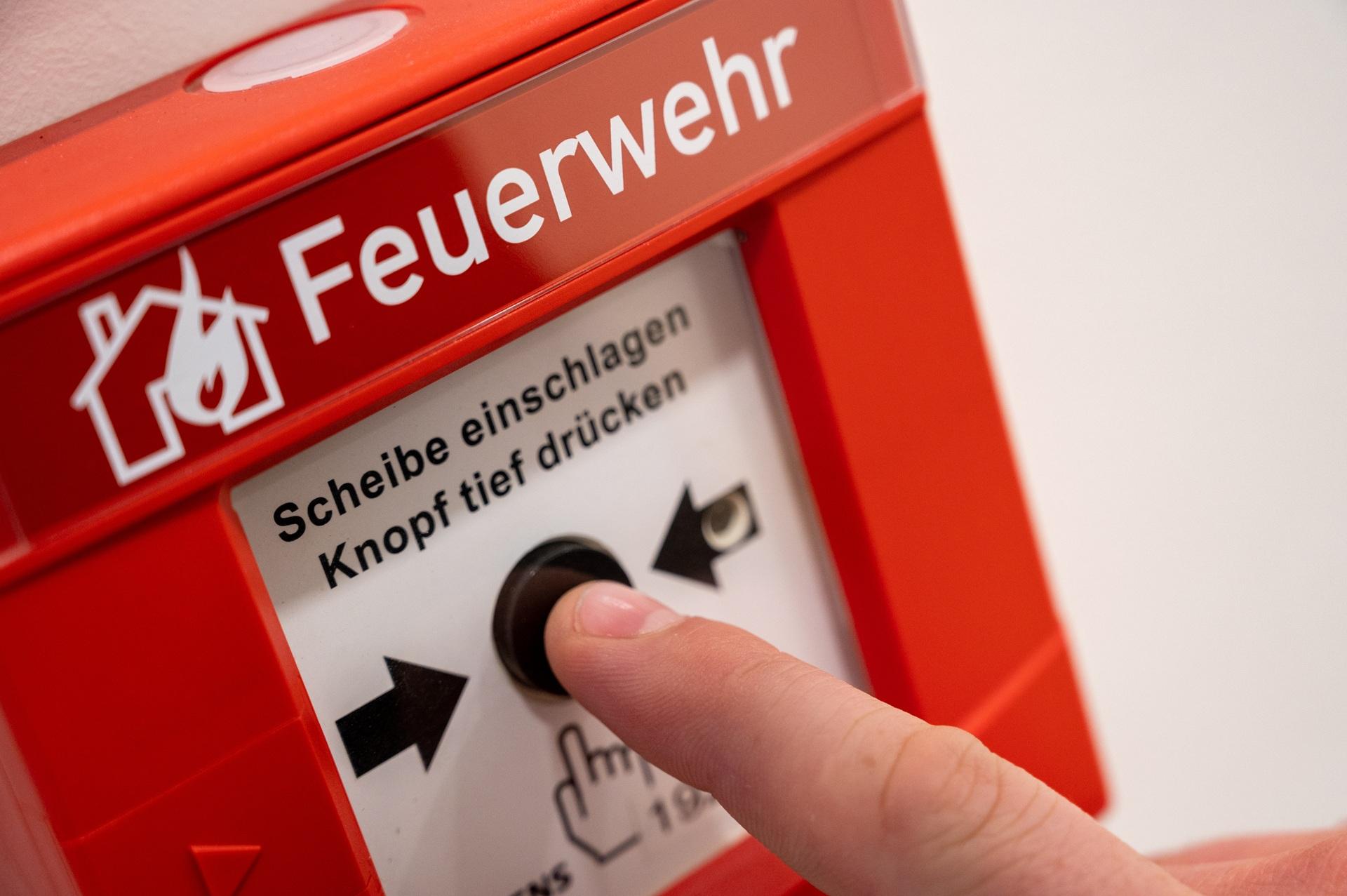 Finger drückt roten Feueralarm-Taster im Gebäude | Brandwache Berlin